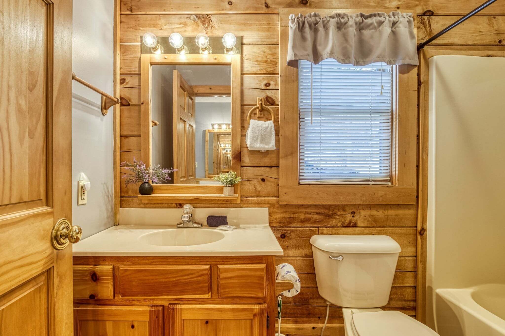 A wooden cabin bathroom with a vanity, sink, mirror, and toilet.