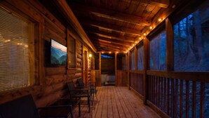 A wooden cabin with a porch, chairs, and a TV screen. - ER204 - Dream Catcher  Great location! - Close to town! (Pigeon Forge)
