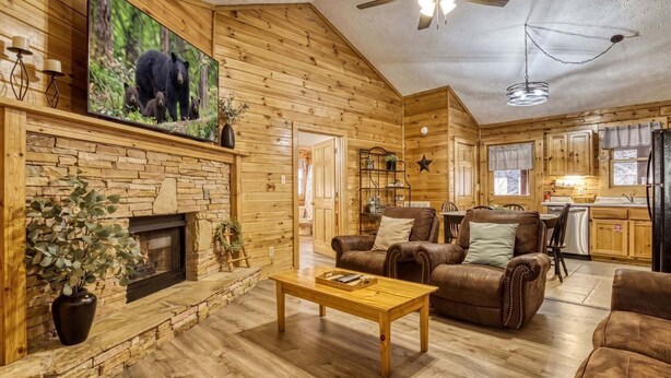 A log cabin interior with a fireplace, leather furniture, a television, and a kitchen area. - ER204 - Dream Catcher  Great location! - Close to town! (Pigeon Forge)