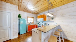 Une cuisine avec des lambris en bois, un réfrigérateur bleu, des armoires orange et un plan de travail en granit.