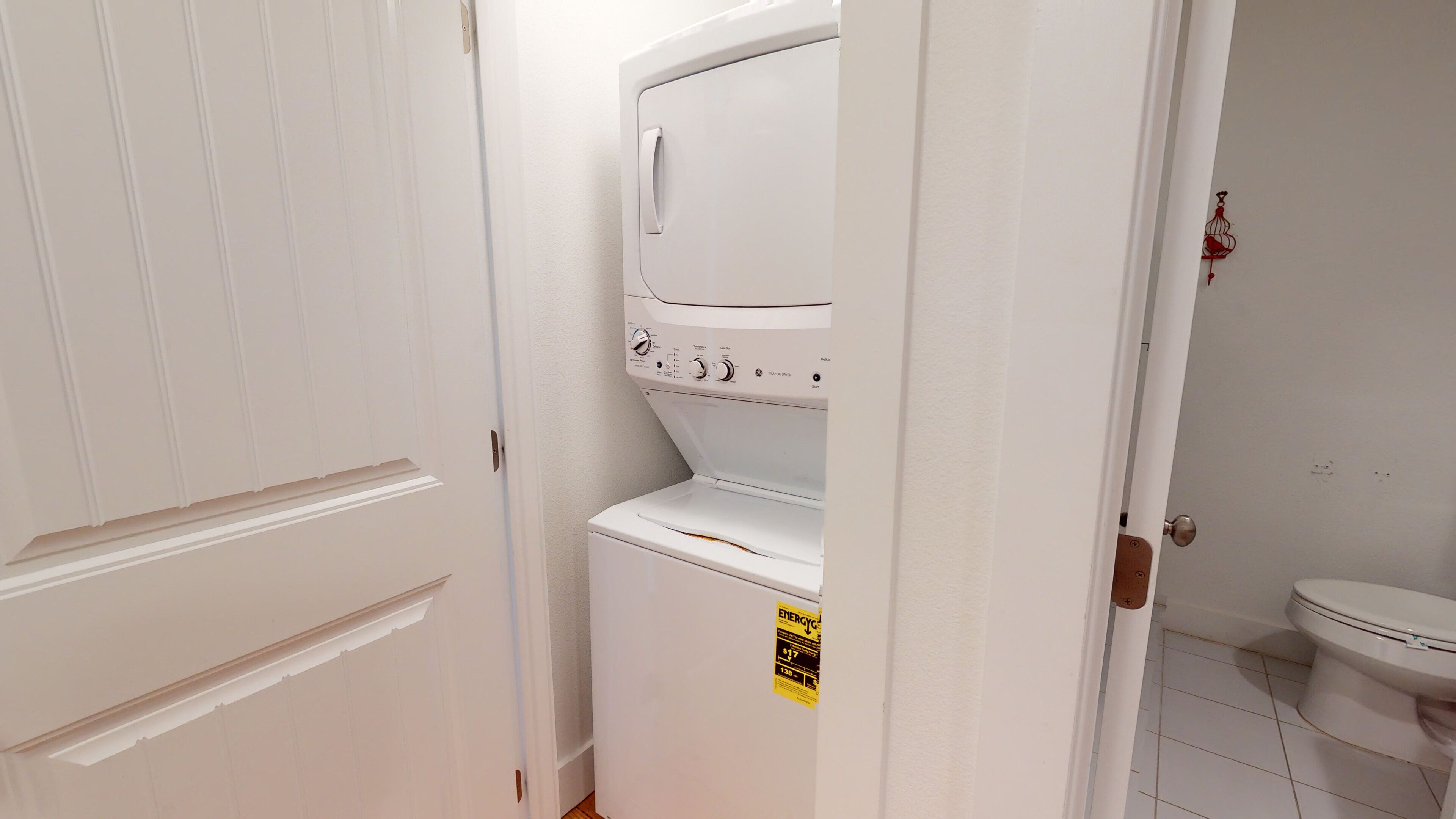 A compact laundry room with a front-loading washer and dryer, a door with a handle, and a toilet visible in the adjacent bathroom.