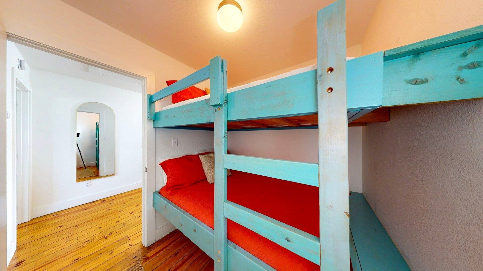 Une chambre avec un lit superposé, un plancher en bois et des murs blancs.