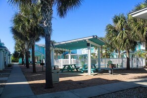 Una località balneare con un'area picnic coperta, palme e case sulla spiaggia.