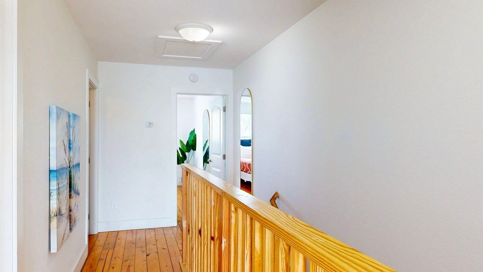 A hallway with a wooden railing, a painting on the wall, and a door leading to another room.