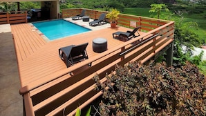 A wooden deck with a swimming pool, lounge chairs, and a view of a green landscape with hills. - Villa 1: Your Perfect Island Family Retreat (Gros Islet)