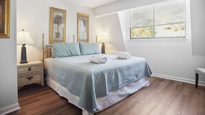 Ein Schlafzimmer mit einem Bett, zwei Nachttischen mit Lampen, einem Fenster mit Jalousien und gerahmten Bildern an der Wand.
