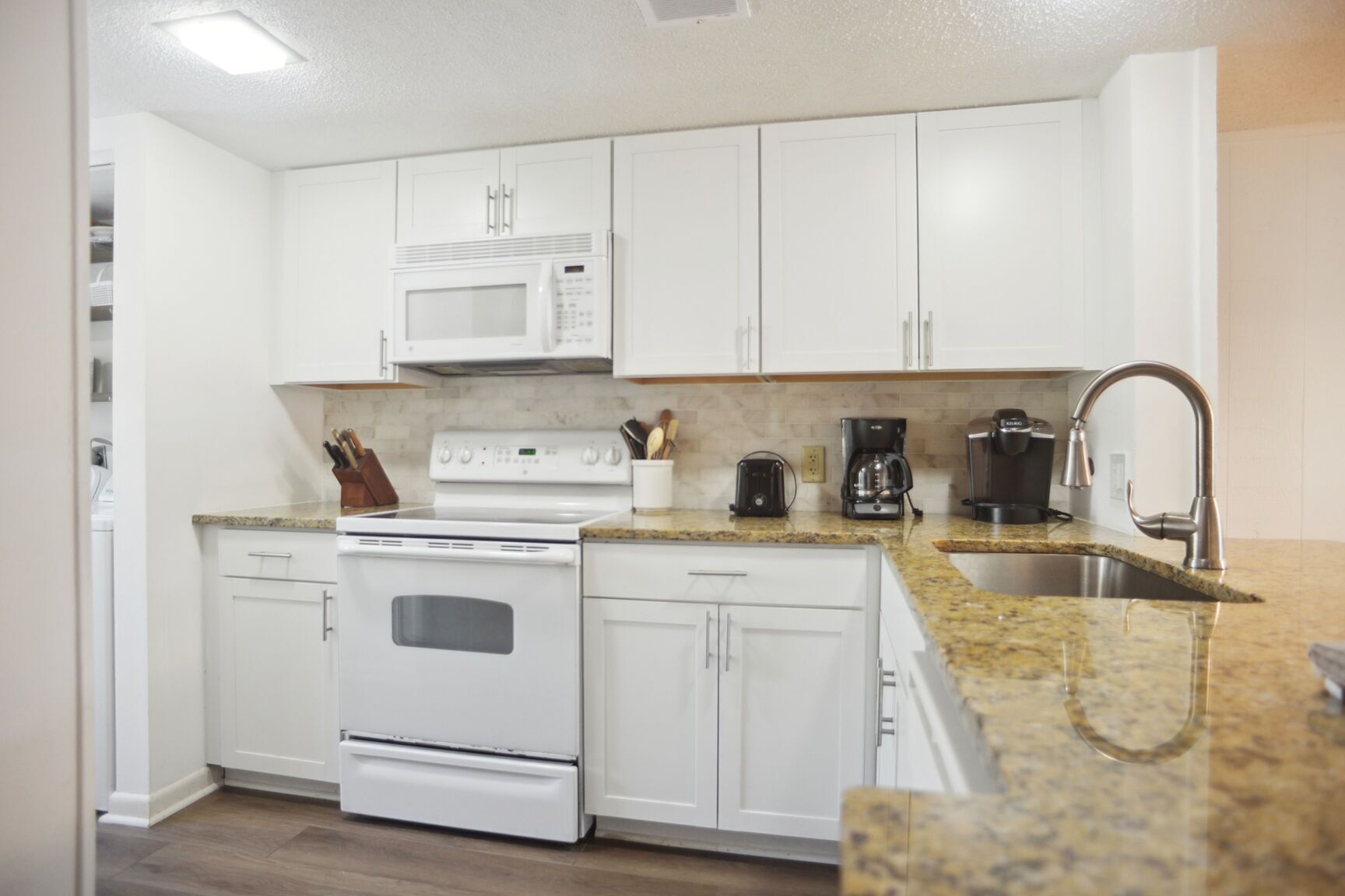 A modern kitchen with white cabinets, a built-in microwave, a stove, a coffee maker, and a sink.