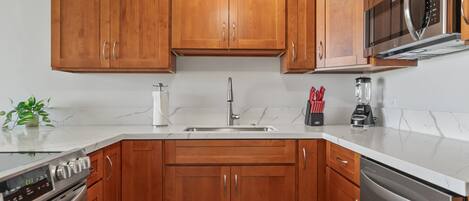 Een moderne keuken met houten kastjes, roestvrijstalen apparatuur en een marmeren aanrecht.