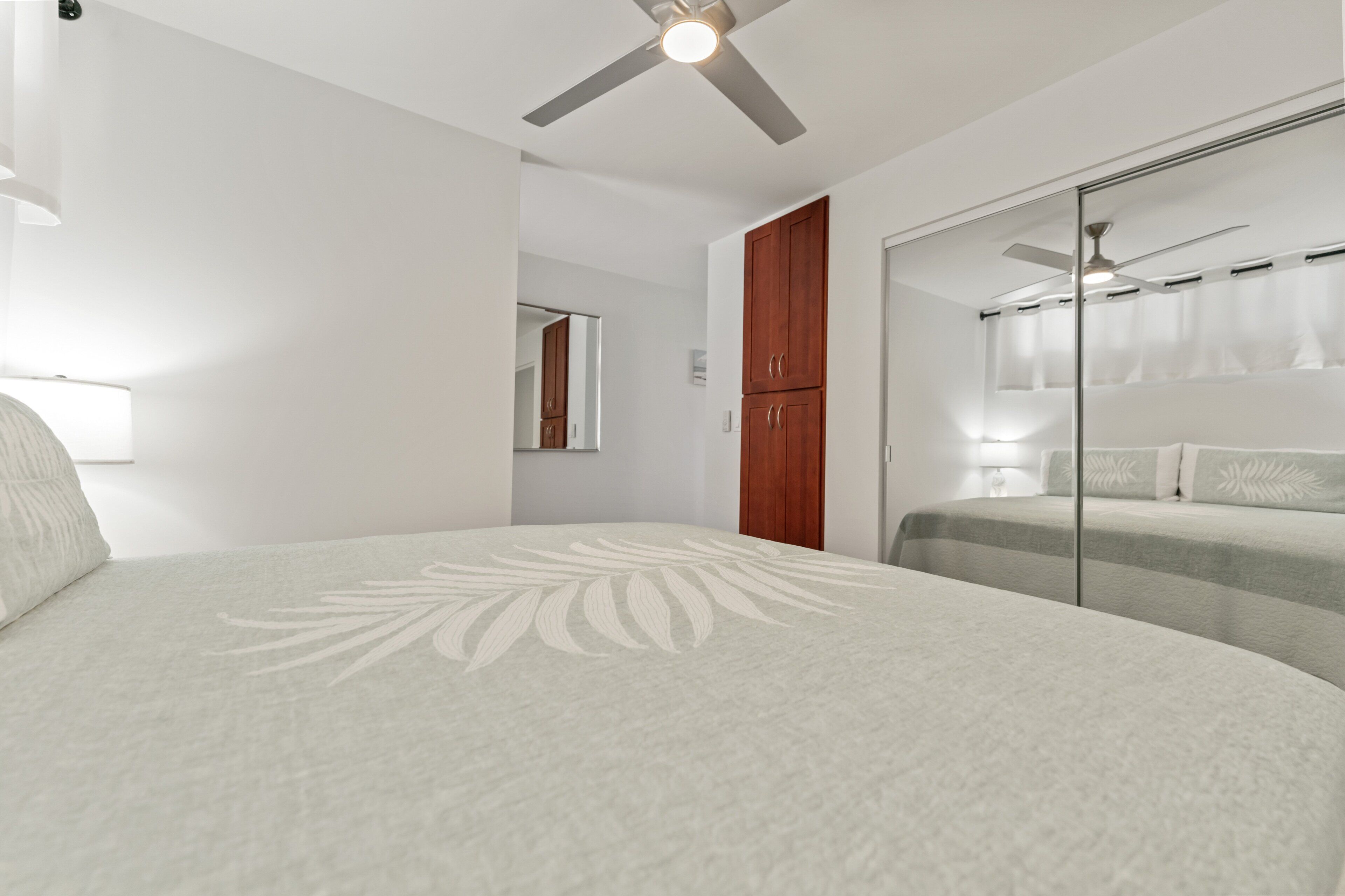 Quarto com cama, ventoinha no teto, guarda-roupa e espelho.