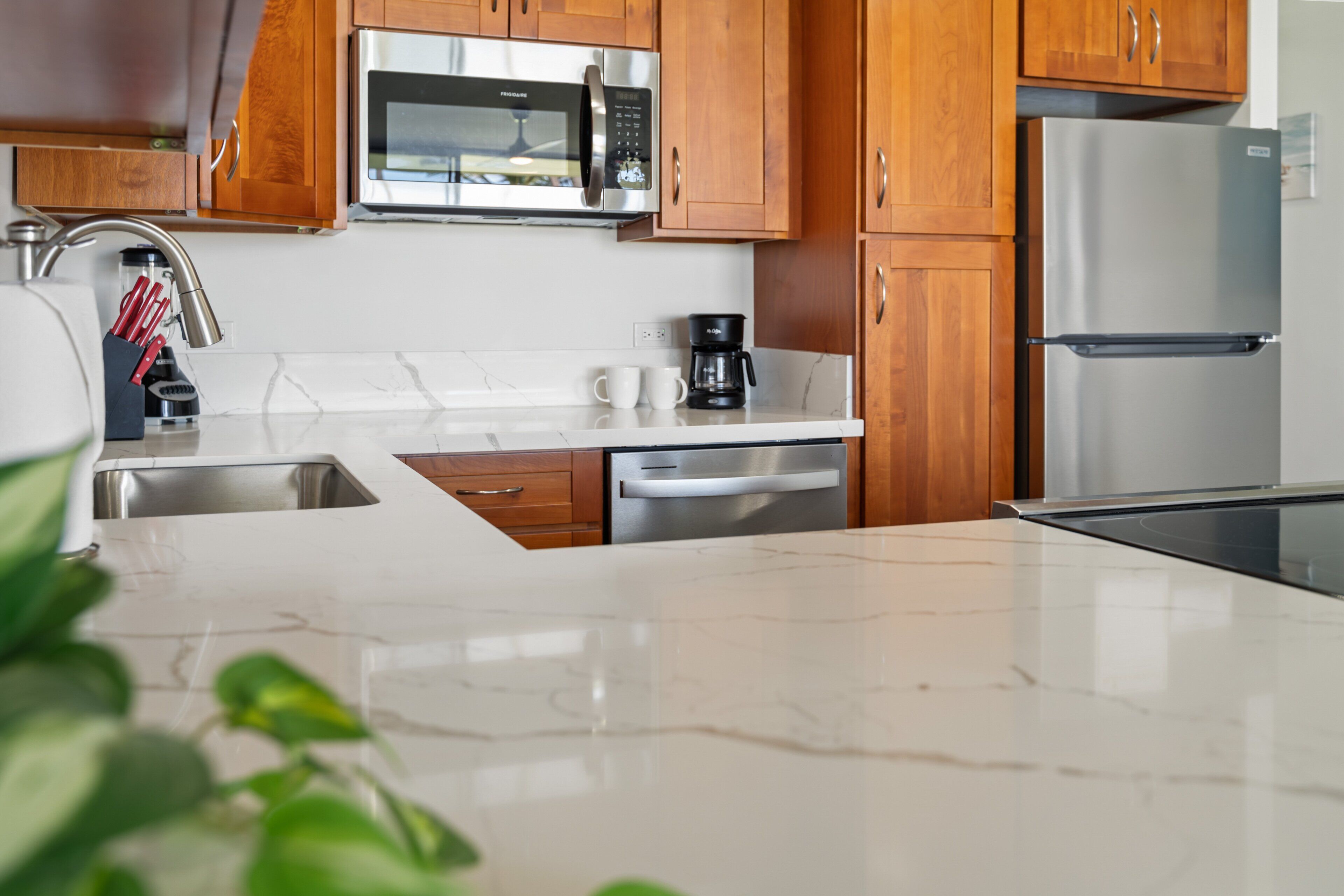 A modern kitchen with wooden cabinets, a stainless steel microwave, a refrigerator, and a coffee maker.
