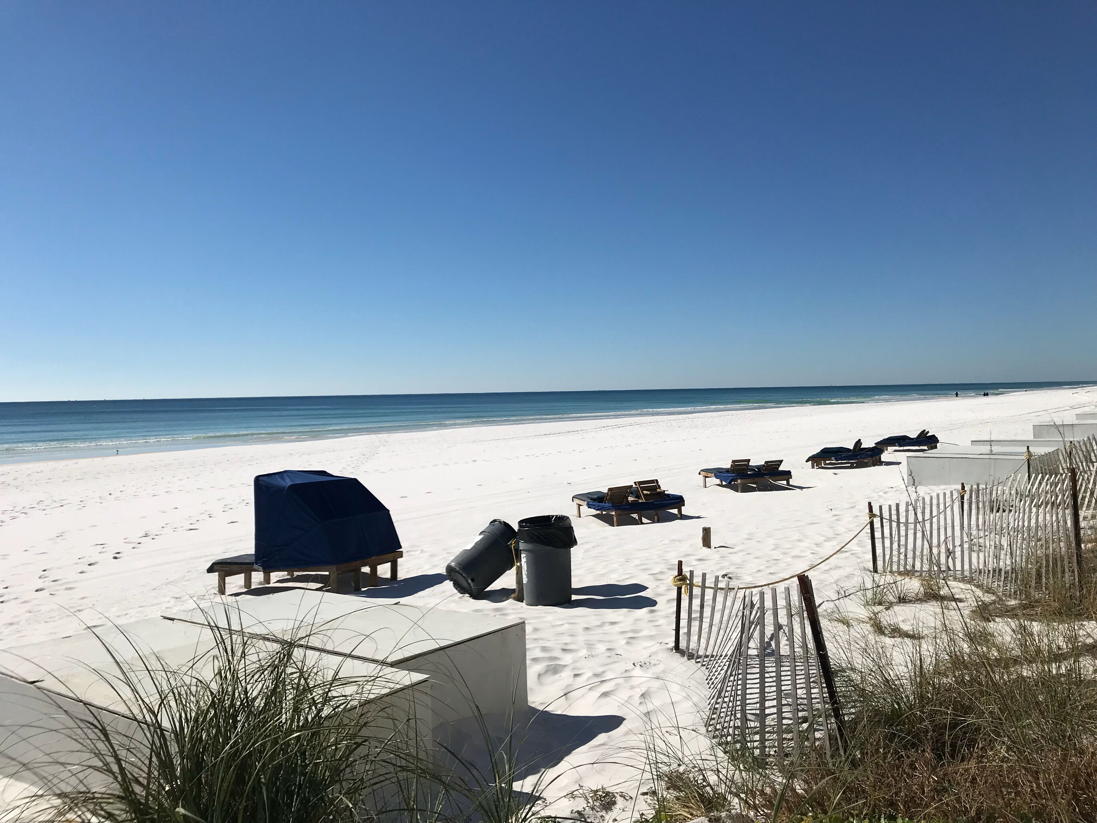 A beach with sun loungers and umbrellas, a wooden fence, and a clear sky.