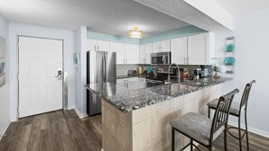 Een moderne keuken met granieten werkbladen, roestvrijstalen apparatuur en een centraal eiland met barstoelen.