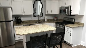A modern kitchen with white cabinets, a granite countertop, a stainless steel refrigerator, a stove, and two black bar stools. - NEWPORT INN #1 - NO CLEANING FEES!! FREE PARKING!! WALK TO GAMES AND CONCERTS!! (Newport)