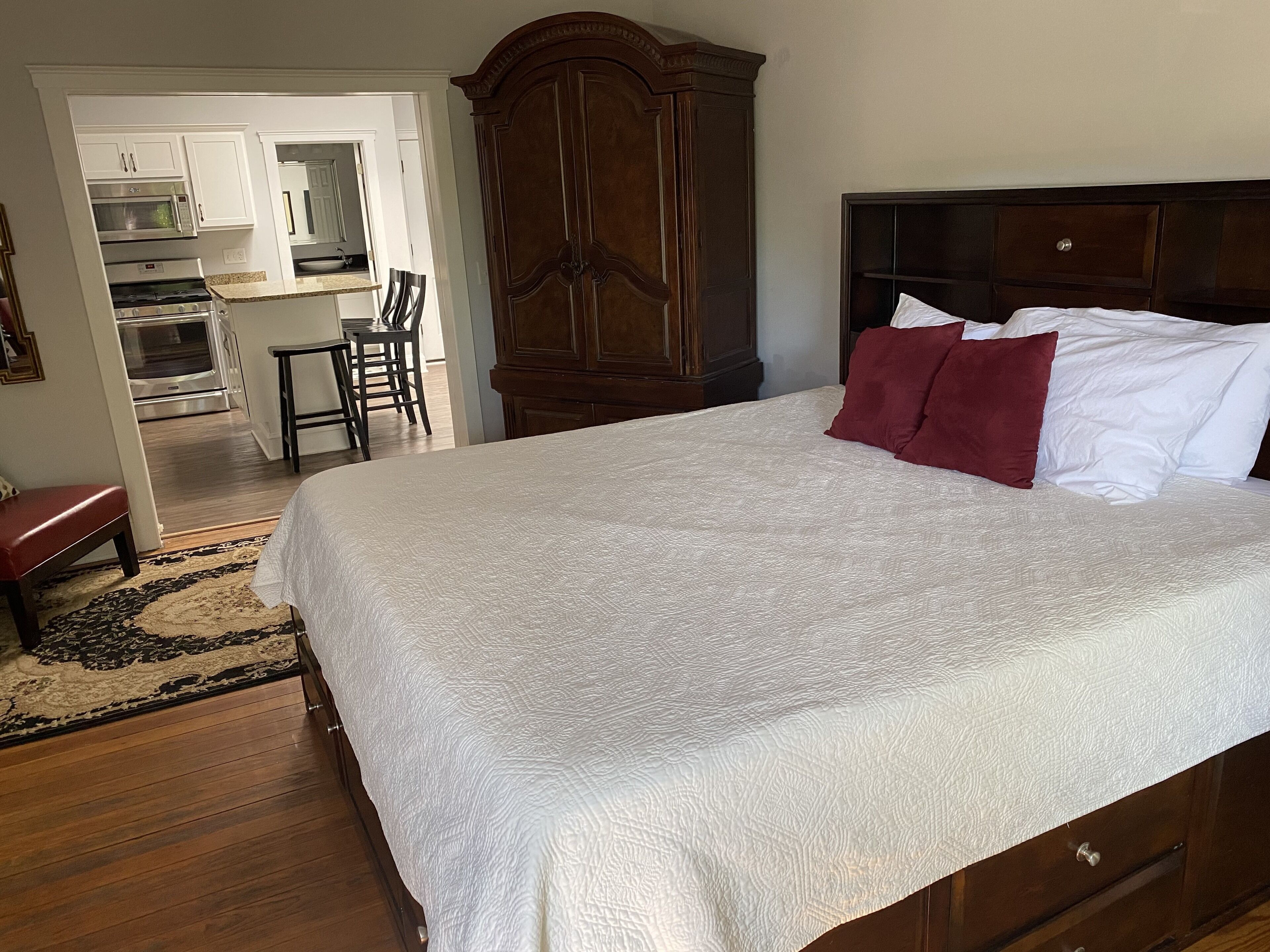 Un dormitorio con una cama grande, un armario de madera y vistas a una cocina y comedor.