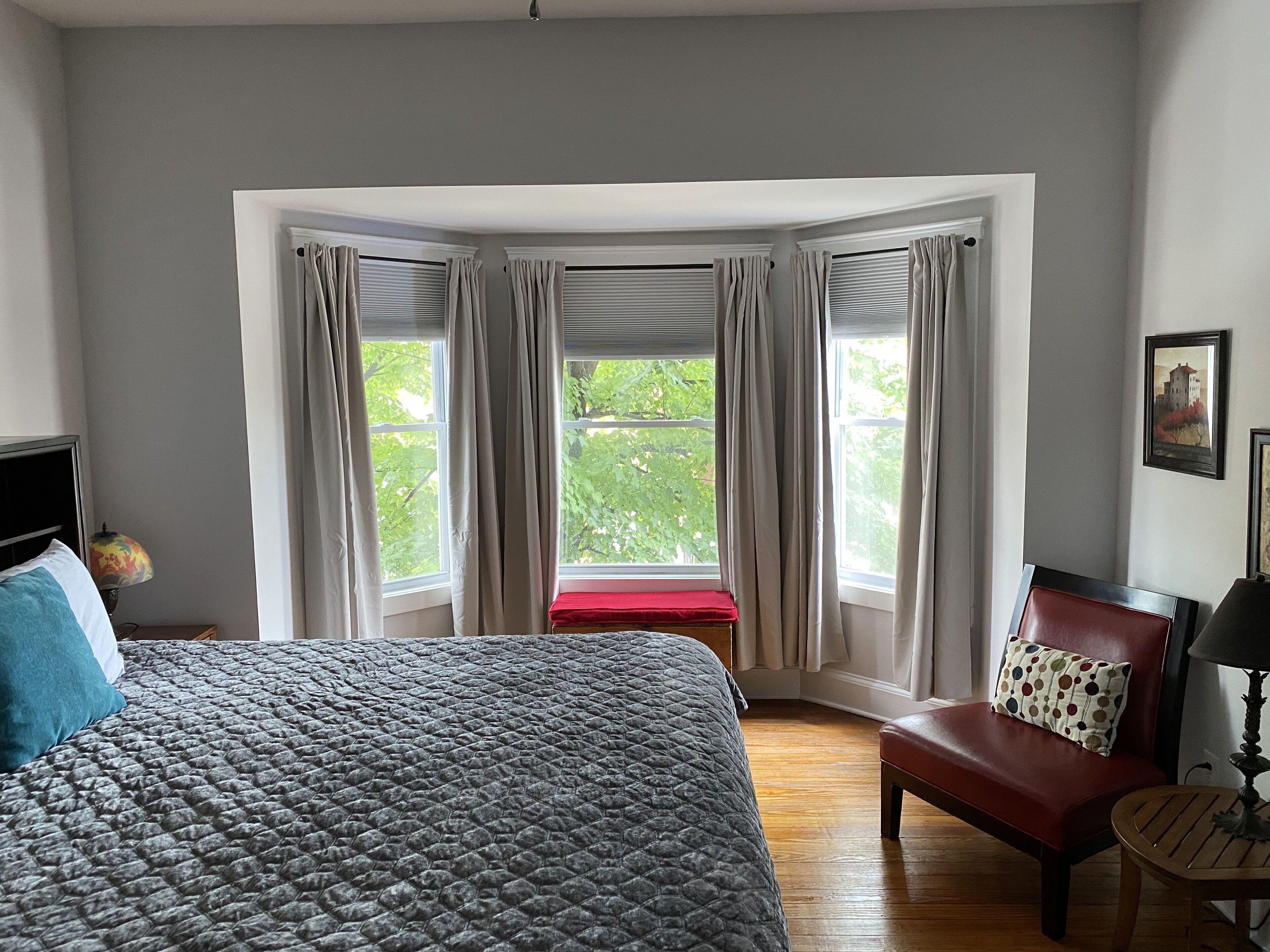 A bedroom with a large bed, a red bench, a wooden chair, and a table.