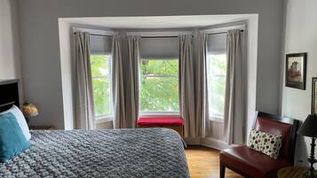 A bedroom with a large bed, a red bench, a wooden chair, and a table.