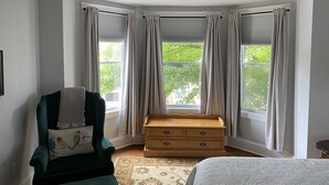 A room with a corner bed, a wooden chest of drawers, a green armchair with a colorful pillow, and a window with curtains. - NEWPORT INN #1 - NO CLEANING FEES!! FREE PARKING!! WALK TO GAMES AND CONCERTS!! (Newport)