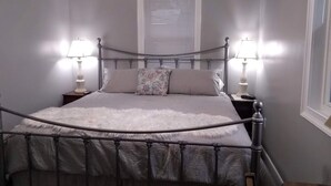 Un dormitorio con una cama de estructura metálica, dos lámparas de noche, una ventana con persianas y una pared blanca.