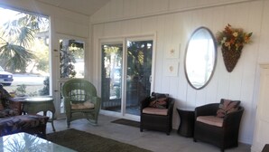 Habitación iluminada por el sol con muebles de mimbre, una mesa de vidrio y un amplio ventanal corredizo que da al exterior.