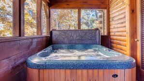 Une cabane en bois avec un jacuzzi au centre, de grandes fenêtres et une porte sur le côté droit.