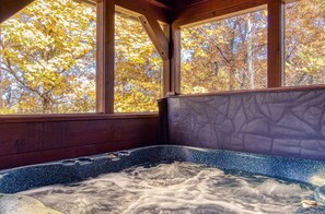 A hot tub with a view of autumn trees through large windows.