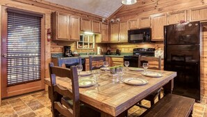L’intérieur d’une cabane en bois comprend une table à manger pour quatre personnes, des armoires en bois, un réfrigérateur noir et un four à micro-ondes.