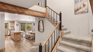 A modern interior with a wooden staircase, a kitchen with wooden cabinets, and a dining area with a large table and chairs. - Luxury! Pool Table! Hot Tub! Pet Friendly! Covered Deck! 4 Master Suites! Log Features! (Big Bear City)