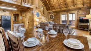 A wooden cabin interior with a dining area set for four, a sofa, a television, and a fireplace.