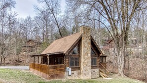 A log cabin with a stone chimney, wooden deck, and a stone staircase leading to the entrance.
