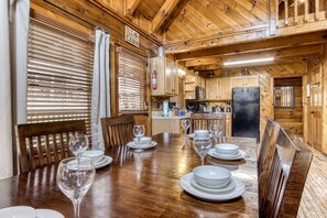 A wooden cabin interior with a dining table set for six, wooden cabinets, a kitchen area, and a sign that reads "All you need is love and a cabin." - ER47 - Moody Blue - Great location. Close to all the action! (Pigeon Forge)