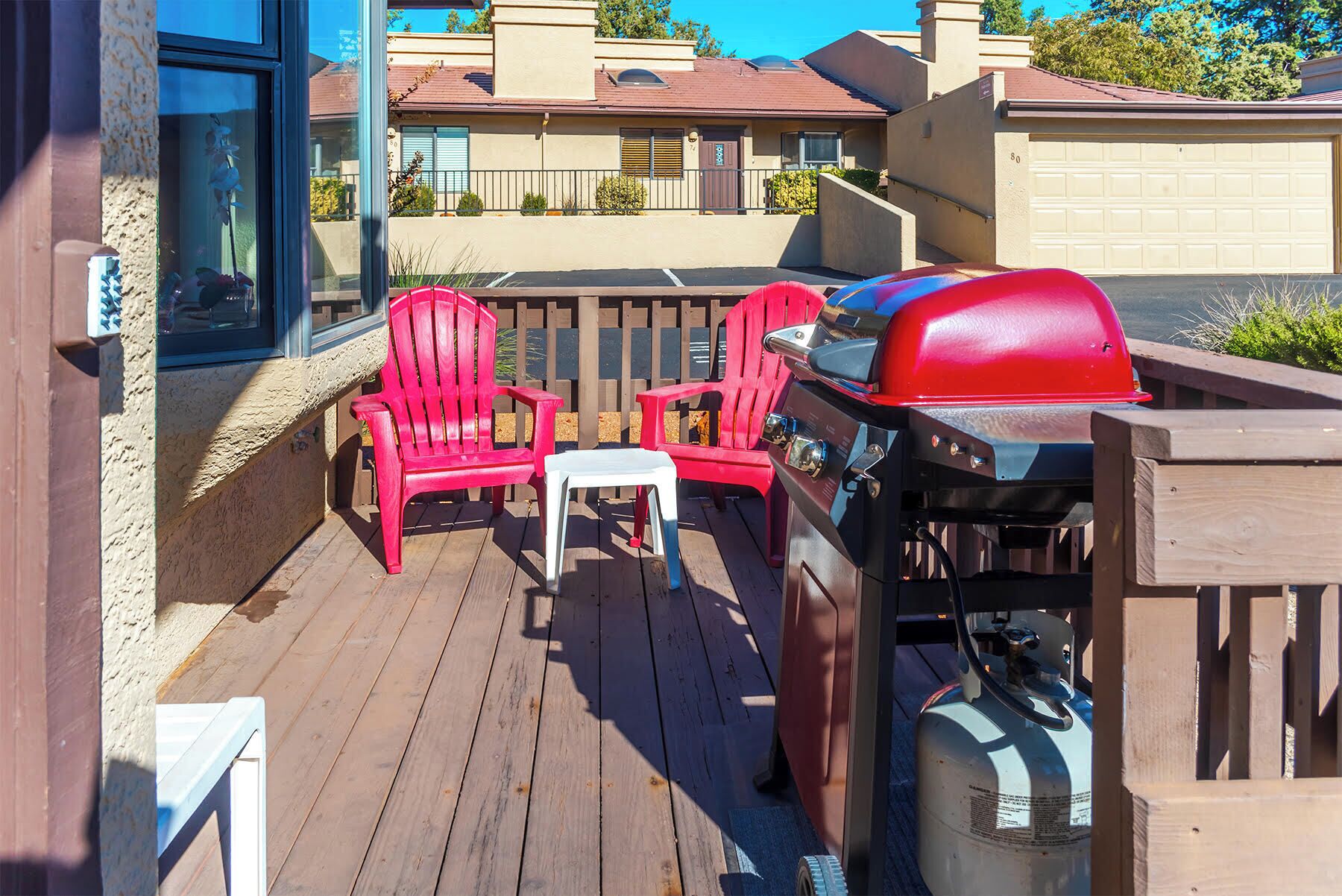 Une terrasse avec un barbecue, deux fauteuils Adirondack rouges et une petite table.