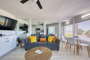 A modern living room with a sofa, coffee table, dining area, kitchen, and TV.