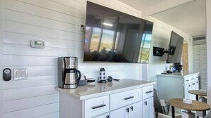 Una cocina moderna con un televisor de pantalla plana grande, una cafetera y un pequeño comedor.