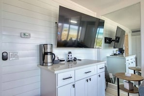 A modern kitchen with a large flat-screen TV, a coffee maker, and a small dining area.