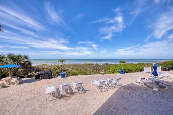 A beachside patio with lounge chairs, a barbecue area, and a view of the ocean.