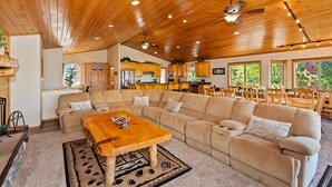 A spacious living room with a large L-shaped sectional sofa, a wooden coffee table, and a dining area with wooden chairs and a table.