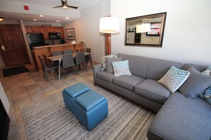 Un salon avec un canapé gris, un pouf bleu et un tapis à motifs.