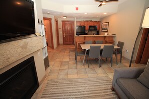 A modern kitchen with a dining area, a flat-screen TV mounted above the fireplace, and a ceiling fan. - Copper One 4th Floor—New Carpet, New Furniture, 2 King Beds (Copper Mountain)