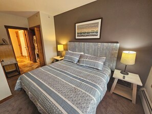 A neatly arranged bedroom with a large bed, a bedside table with a lamp, and a framed picture on the wall. - Copper One 4th Floor—New Carpet, New Furniture, 2 King Beds (Copper Mountain)
