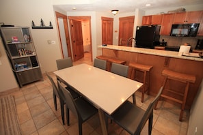 A kitchen with a dining table, chairs, wooden cabinets, a refrigerator, and a microwave. - Copper One 4th Floor—New Carpet, New Furniture, 2 King Beds (Copper Mountain)