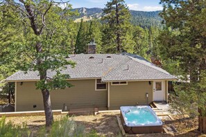 A single-story house with a sloped roof, a hot tub, and a view of a forested mountain range.