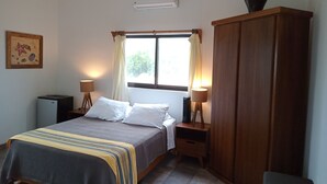 Un dormitorio con cama, lámparas de noche, armario, una mesita y aire acondicionado instalado en la pared.