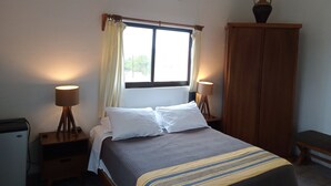 Un dormitorio ordenado con cama, lámparas de noche, armario y ventana con cortinas.