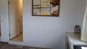 Un pasillo con una puerta que da a una habitación, un cuadro con una escena costera y una pequeña mesa con un farol.