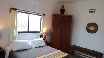 A bedroom with a bed, a bench, a wardrobe, a lamp, and a window with curtains.