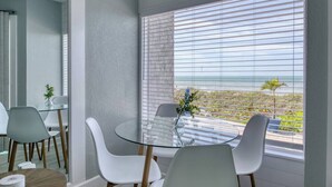 A modern room with a glass table, white chairs, and a view of the ocean through large windows.