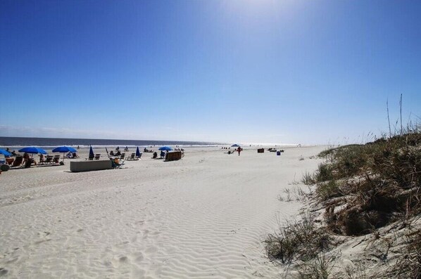 A beach with sand, blue umbrellas, and beach chairs.