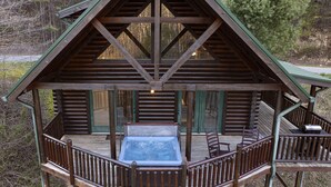 A wooden cabin with a hot tub on a deck, surrounded by trees.