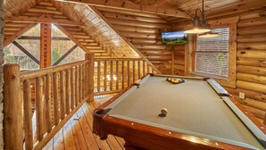 A wooden cabin with a pool table, wooden railings, and a television mounted on the wall.