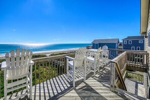Eine Holzterrasse mit weißen Adirondack-Stühlen mit Blick auf einen Strand.